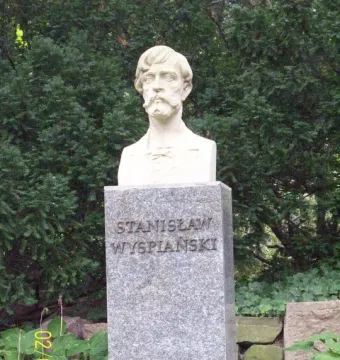 Stanisław Wyspiański bust on a tall granite pedestal surrounded by green foliage.