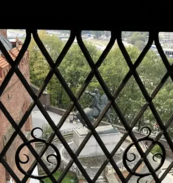 Tadeusz Kościuszko Monument seen through a dark window grate, showing a bronze equestrian statue on a pedestal.