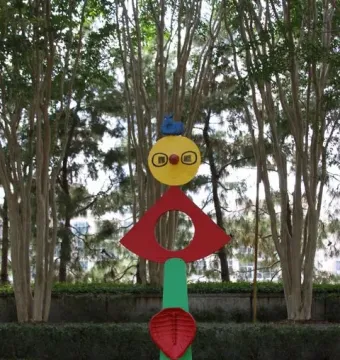 The Caress of a Bird sculpture with stacked brightly colored shapes in a garden setting.