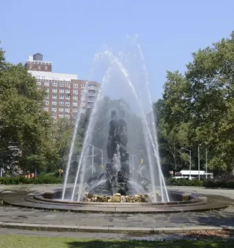 Bailey Fountain with water arcing around dark metallic statues in a circular stone basin.