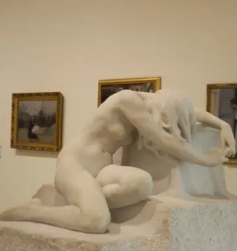 Desolation, a white marble nude female sculpture crouching with her head bowed beside a rough stone base.