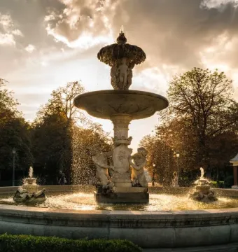 Fountain of the Artichoke in a park, with water cascading from the stone tiers into a circular pool at sunset.