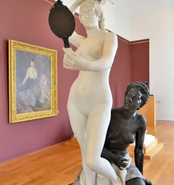 Le Miroir sculpture showing a white marble nude woman holding a hand mirror above a kneeling bronze figure on a decorative base.
