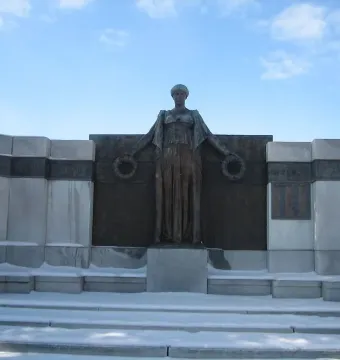 Soldiers\' Monument bronze figure holding wreaths in front of a curved stone structure with snowy steps.