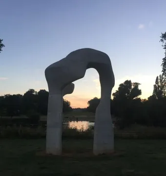 The Arch stone sculpture frames a sunset over water and trees.