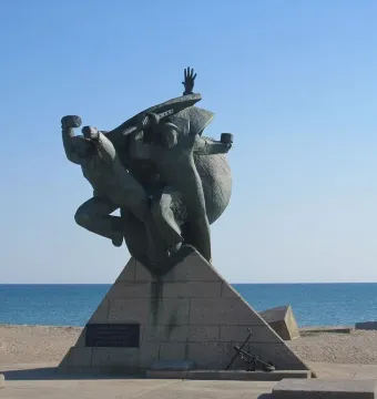Monument of Eupatoria Assault bronze sculpture with three figures on a stone base by the sea.