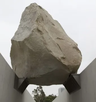Levitated Mass shows a massive boulder suspended above a concrete pathway between sloping walls.