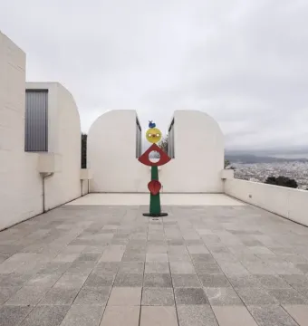The Caress of a Bird sculpture with stacked green, red, and yellow shapes topped by a small blue bird in a courtyard.