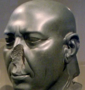 Berlin Green Head stone sculpture with a bald head, carved wrinkles, and a broken nose on a stand.