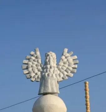 Colonne Pascale with a white winged figure above a spherical base beside a tall yellow stacked column.