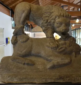 Weathered Corbridge Lion sandstone sculpture of a lion standing over a recumbent animal indoors.