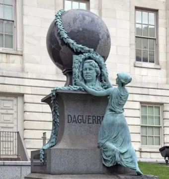 Daguerre Memorial showing a bronze figure kneeling beside a bust, with a garland and globe above the pedestal.