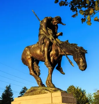 End of the Trail bronze sculpture of a bowed rider on a weary horse against a blue sky.