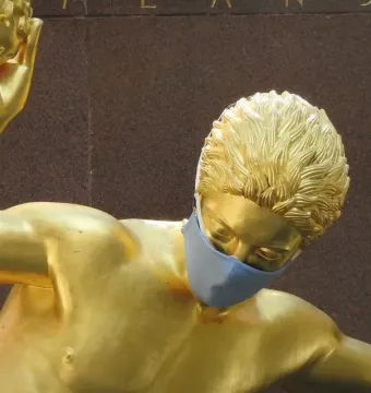 Masked Prometheus gilded statue with an arm raised and holding a golden object.