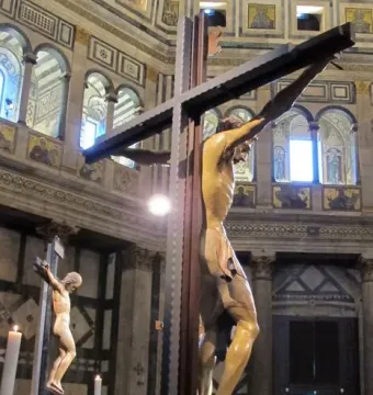 Santa Croce Crucifix displayed inside an ornate church interior, with a smaller crucifix, visitors, and tall candles in the background.