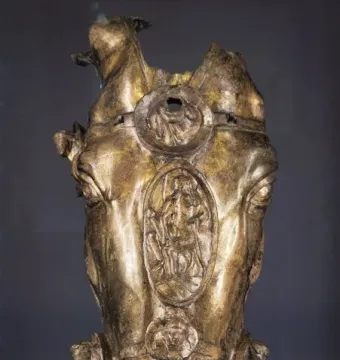 Weathered golden horse head sculpture with three decorated medallions down the center.