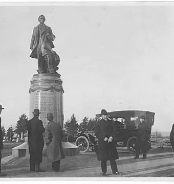 William Henry Seward monument in Volunteer Park with several men gathered around the base and a vintage automobile nearby.