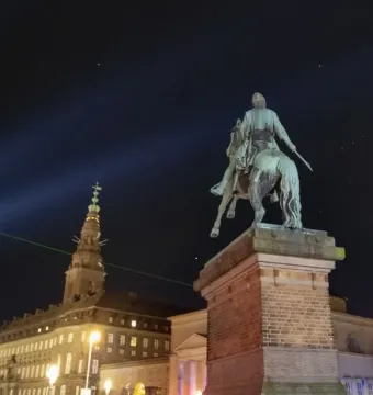 Absalon Monument silhouetted at night with illuminated buildings in the background.