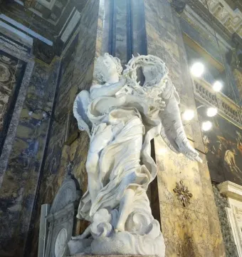 Bernini\'s Angel with the Crown of Thorns in white marble, holding a thorny wreath inside a richly decorated church interior.