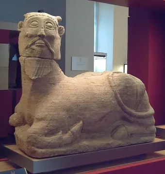 Bicha of Balazote sculpture with a human head and bovine body reclining on the ground.
