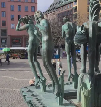 Orpheus Fountain with greenish-bronze nude statues in a city square.