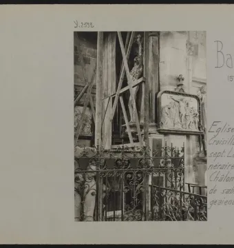 The Transi of René of Chalon skeletal stone sculpture stands behind an ornate iron fence, with wooden braces supporting it.