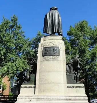 Rear view of the von Steuben statue on a tall stone pedestal with reliefs on the base.