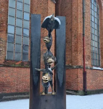 Bremer Stadtmusikanten sculpture with stacked donkey, dog, cat, and rooster on snowy ground beside a brick building.