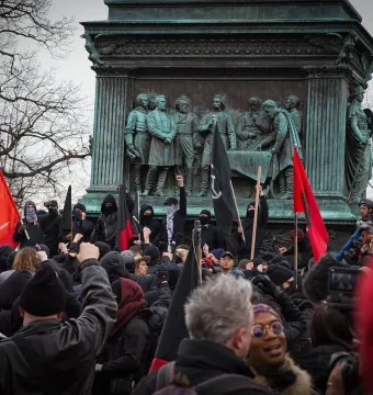 Crowd gathered around the Major General John A. Logan monument, with raised fists and red and black flags in front of the bronze sculpture.