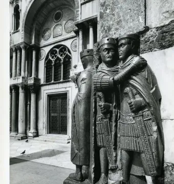 Portrait of the Four Tetrarchs, a dark carved group of four figures embracing, set before an ornate arched building.