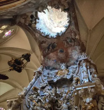 The Transparente in Toledo Cathedral, showing a richly carved Baroque altarpiece beneath a circular ceiling opening with painted celestial scenes.