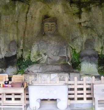 Usuki Stone Buddhas carved into a rock face, with a central seated figure and smaller figures nearby beside offerings and a wooden fence