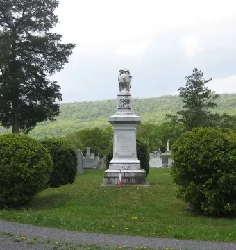 Confederate Memorial stone monument topped with a draped figure holding an urn in a cemetery.