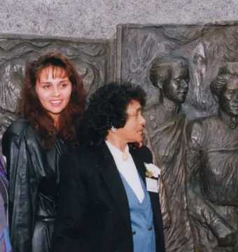 Three women stand in front of the Kate Sheppard National Memorial bronze relief sculpture.