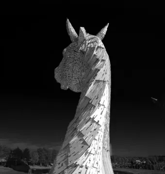 The Kelpies horse head sculpture rising against a dark sky in black and white.