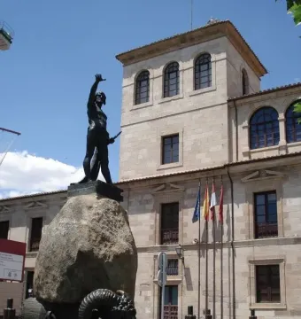 Monument to Viriato showing a dark warrior statue on a rocky base beside a stone building.