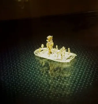 Muisca Raft golden miniature with small figures on a reflective dark surface