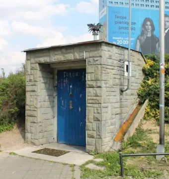 A small stone structure with a blue door beside a paved path.