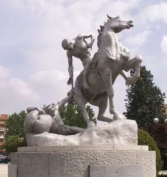 The Torch Bearers stone monument shows a rider on a rearing horse reaching down toward a reclining figure on a rocky base.