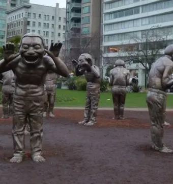 A-maze-ing Laughter sculpture with dark metallic laughing figures in a semicircle outdoors.