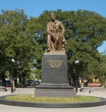The Chekhov monument shows a bronze seated figure holding a book on a dark granite pedestal in a park.