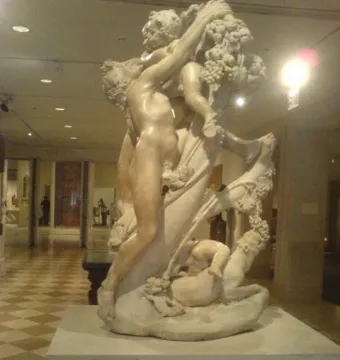 Marble sculpture of A Faun Teased by Children showing a muscular nude figure reaching up toward grapes and a child, with another child near the base.