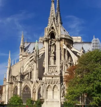 Fontaine de la Vierge monument in front of Notre-Dame Cathedral, with a stepped basin and red flowers at its base.