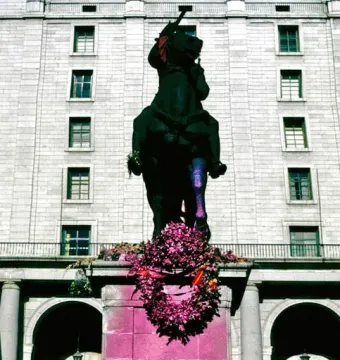 Equestrian statue of Francisco Franco on a stone pedestal covered in bright pink paint, with a purple floral wreath hanging on the front.