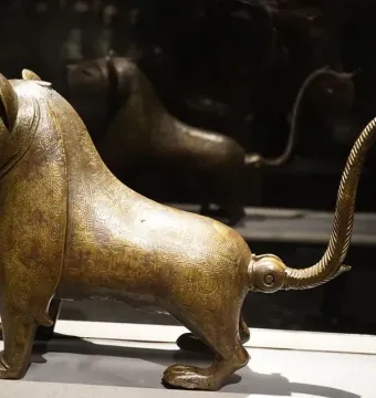 Lion of Monzon sculpture in profile, with engraved patterns and a curled tail.