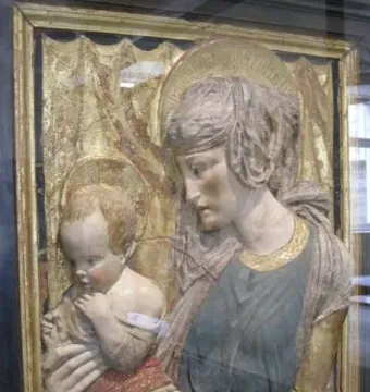 Painted terracotta Madonna and Child relief in a dark frame behind reflective glass.