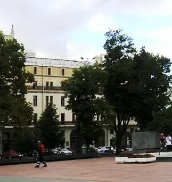 Monument to Karl Marx standing in a paved urban plaza with an illuminated billboard and buildings in the background.