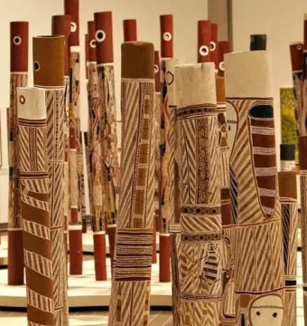 Decorated hollow log tombs from the Aboriginal Memorial stand upright in a dense group, painted with stripes, zigzags, and stylized figures.