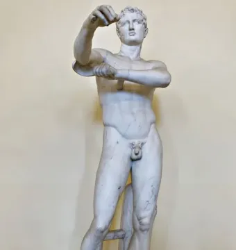 White marble Apoxyomenos statue of a nude male figure standing with one leg bearing his weight and his arms raised.