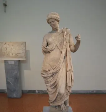 Damaged marble statue of Armed Aphrodite on a pedestal in a museum exhibit.
